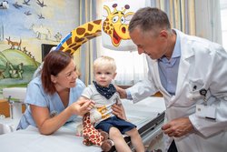 Krankenschwester mit Kleinkind und Primar Oswald in Behandlungszimmer