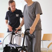 Therapeutin unterstützt einen Patient mit Rollator